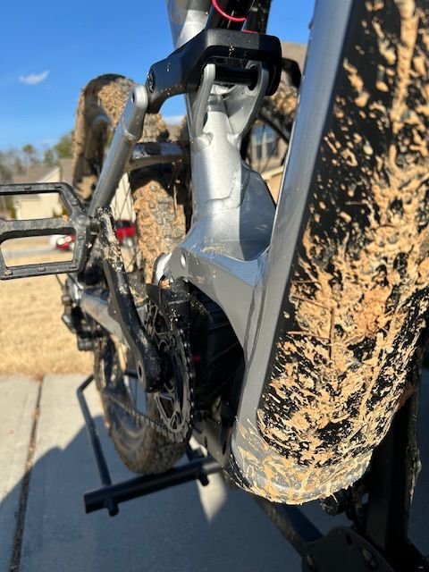 Muddy e-mountain bike picture angled from front of frame with drivetrain and back wheel in the background.