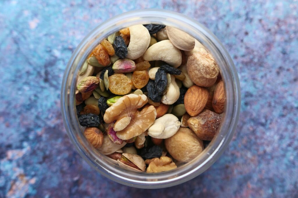 Top view of a variety of nuts and dried fruits in a jar against a blue background.